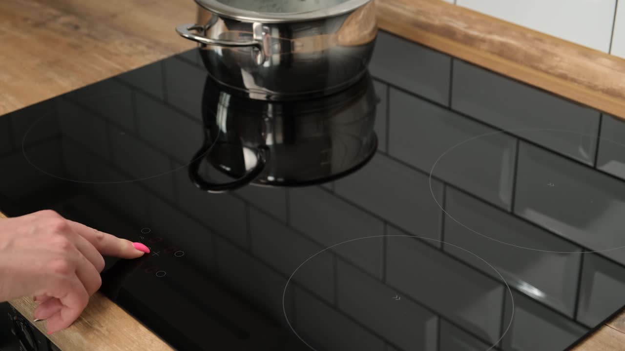 A close-up of a female hand includes an induction hob. Modern technology. Touch panel of electric cooker. Metal pan stands on the touch plate.