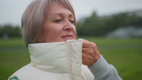 close up of trainer wearing mint green hoodie and gray pants carefully zipping puffy sleeveless coat from bottom to top outdoors on grassy field, preparing for outdoor activity on cool cloudy day