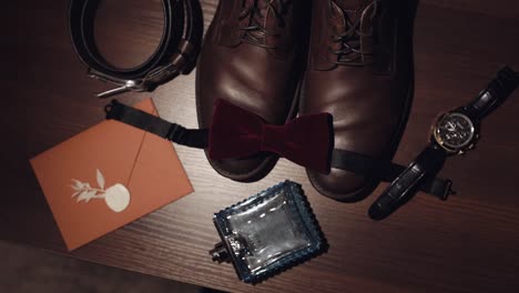 wedding details of groom, bridegrooms perfume, belt, shoes, bow tie, envelope with invitation, clock