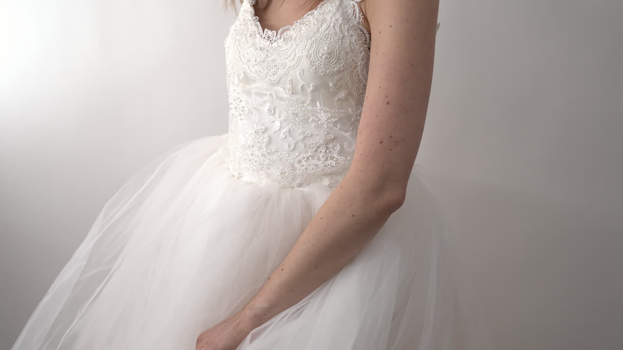 The camera captures a shot of the bride’s elegant white dress. Her hands gently play with the fabric, creating a beautiful flow and movement.