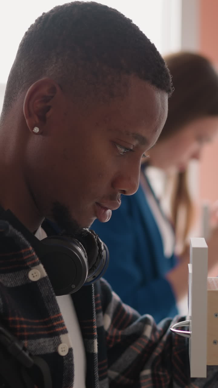 Visitors of library seek for library cards in paper storage. African American man with backpack wearing checkered shirt immersed in card index box. Students turn in books