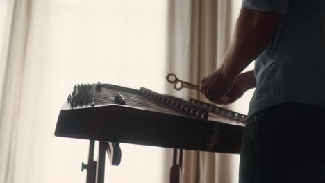 un hombre tocando un instrumento de música clásica tradicional de cuerda dulcimer, parado frente a la ventana con una luz cálida.