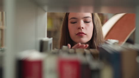 woman looks at books on shelf in library. concentrated student chooses literature materials for essay writing in bookcase closeup. constant reader