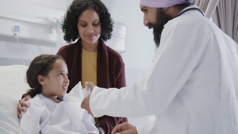 happy biracial doctor using inhaler on sick girl patient with mother in hospital in slow motion