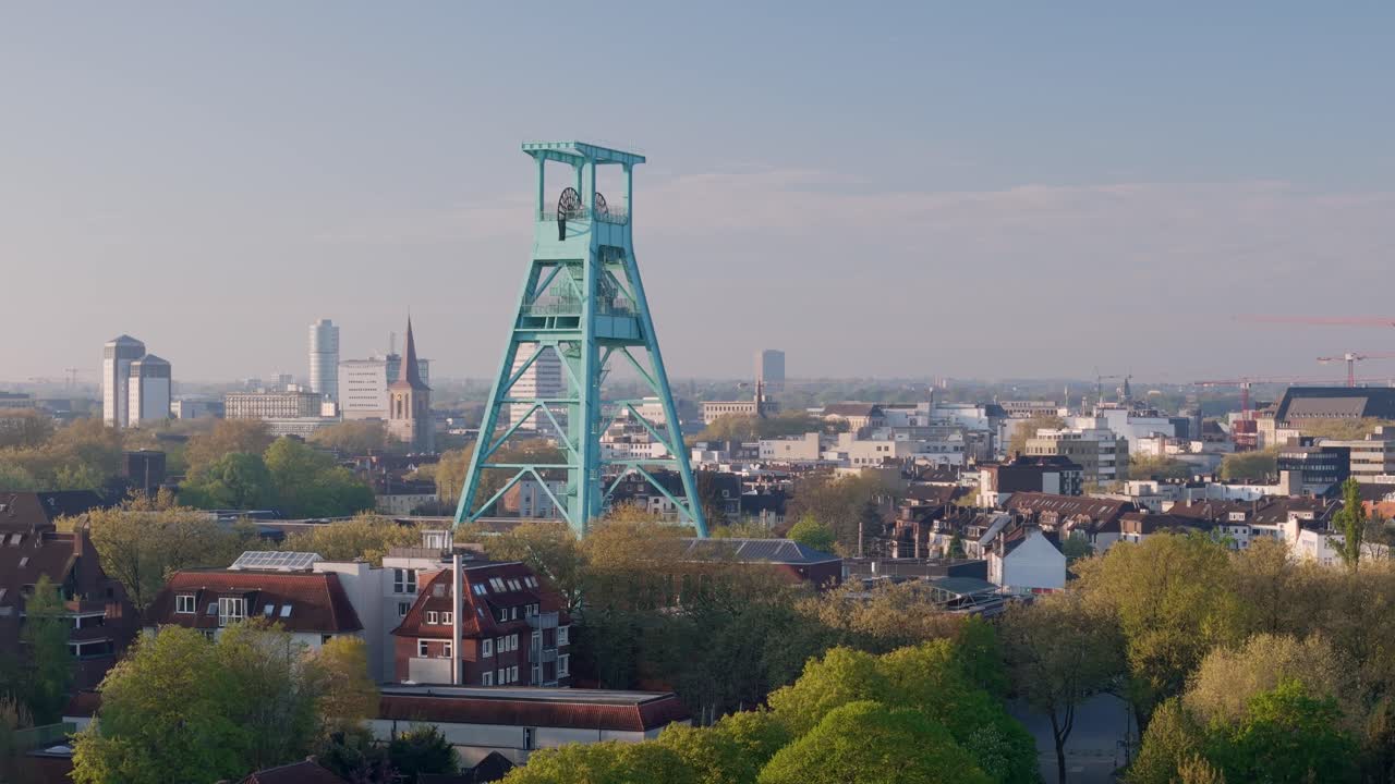Bochum, German Mining Museum, old coal mine shaft, with city skyline in background, warm pastel morning light, clear sky