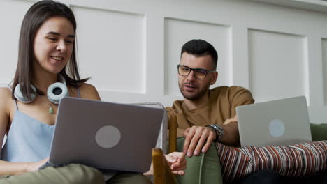 student talking with female mate sitting on sofa while looking at laptop 1