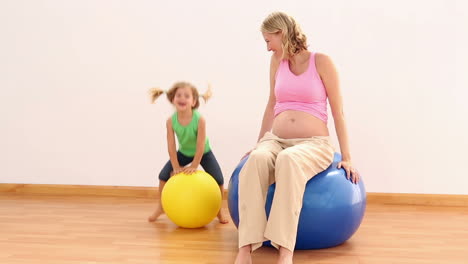 blonde pregnant woman sitting on exercise ball with her little girl