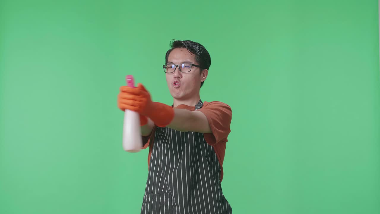 녹색 스크린 스튜디오에 서 있는 동안 스프레이를 사용하여 전신을 가진 재미있는 아시아 남성 집주인