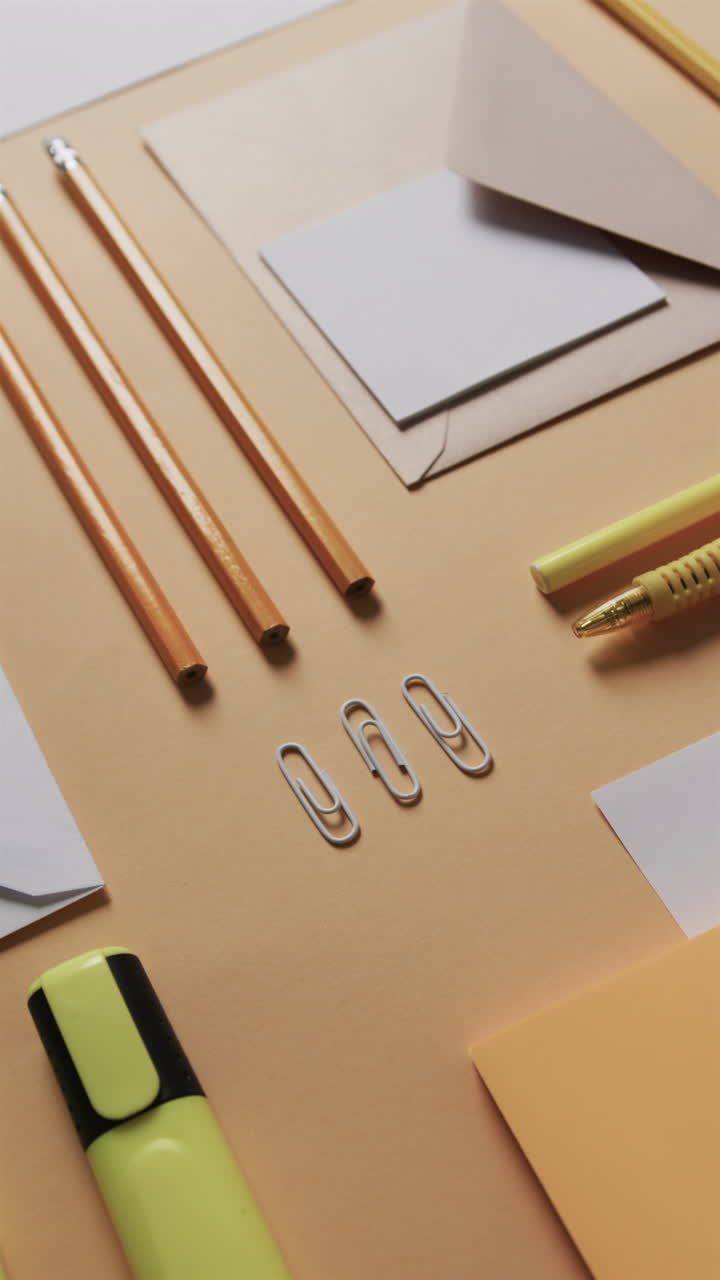 Vertical video of close up of pencils and stationery arranged on beige background, in slow motion