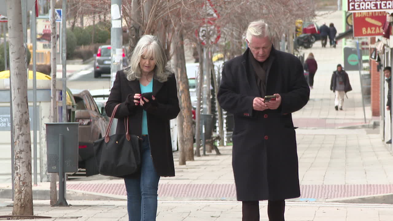 Older couple walking and using smartphones on city street