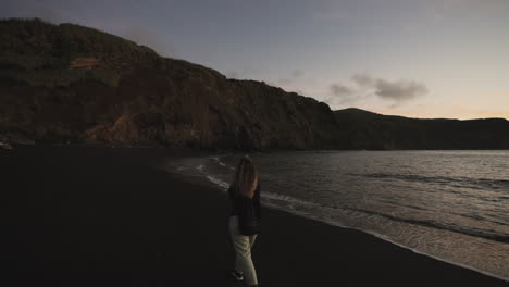 Frau-Geht-In-Der-Abenddämmerung-Am-Strand-An-Den-Klippen-Der-Azoren-Spazieren,-Mit-Breitem-Handheld