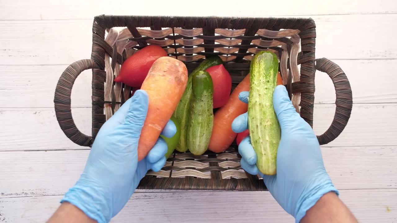 손은 파란 장갑으로 바구니에 채소를 다루고 있습니다.