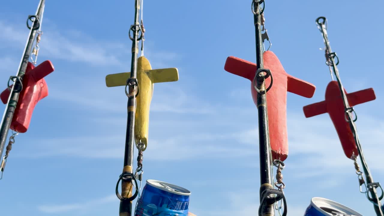 Fishing rods with colorful lures sway gently on a boat against a clear blue sky in Phuket, Thailand