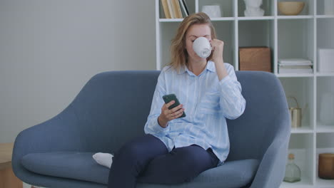 Attractive-redhair-teenager-girl-sitting-of-the-sofa-at-home-using-phone-and-smiling.-Feeling-happy.-Communication-female-looking-message-at-cell-phone-or-smartphone.