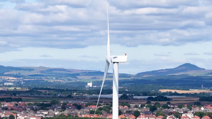 Stor vindmølle snurrer jævnt over hustagene i Dundee i klart dagslys og delvist skyet himmel