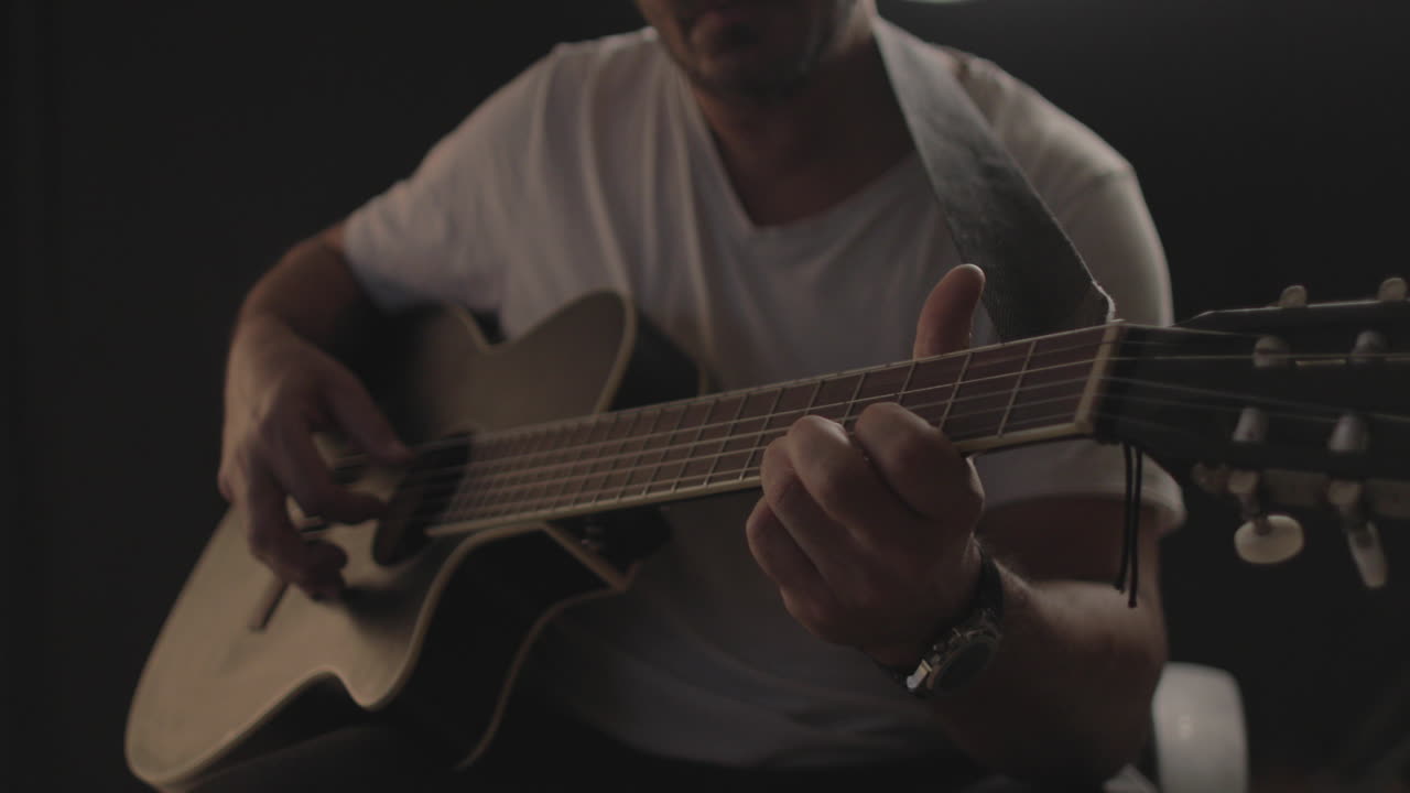 hombre tocando y tocando una guitarra acústica con fondo negro y luz suave y cálida