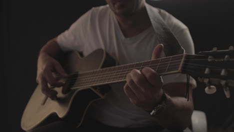 man playing and performing on an acoustic guitar with black background and soft warm light