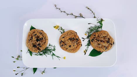 three chocolate chip cookies on a plate with floral arrangement