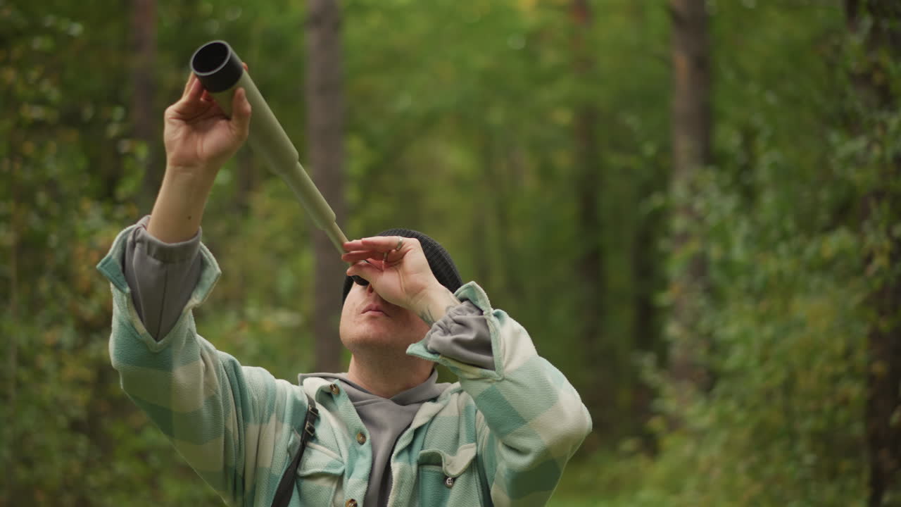 Esploratore che esamina l'attrezzatura, avventuriero che studia il telescopio fatto a mano, utente che ispeziona il cannocchiale artigianale tra i sentieri della foresta, ricercatore che regola attentamente la lente del cannocchiale fatto a mano all'aperto