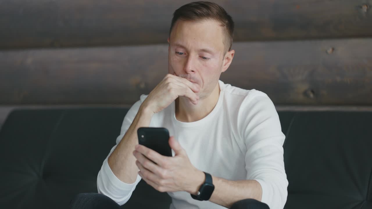 초점을 맞춘 남자는 소파에 앉아서 손에 들고 있는 스마트폰 스크린을 쳐다본다.