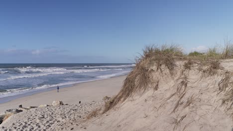 Sand-beach-and-dune,-ocean-in-background-and-walking-people,-static-wide-angle-view