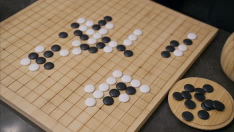 overhead 45 degree view of gameplay in the ancient chinese board game go with a man's hand slowly placing a white stone piece and lingering briefly before committing