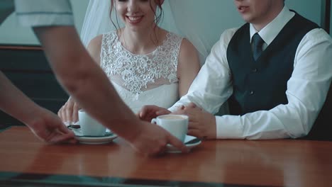 waiter brings coffee mugs to the newlyweds who are sitting in a cafe close-up