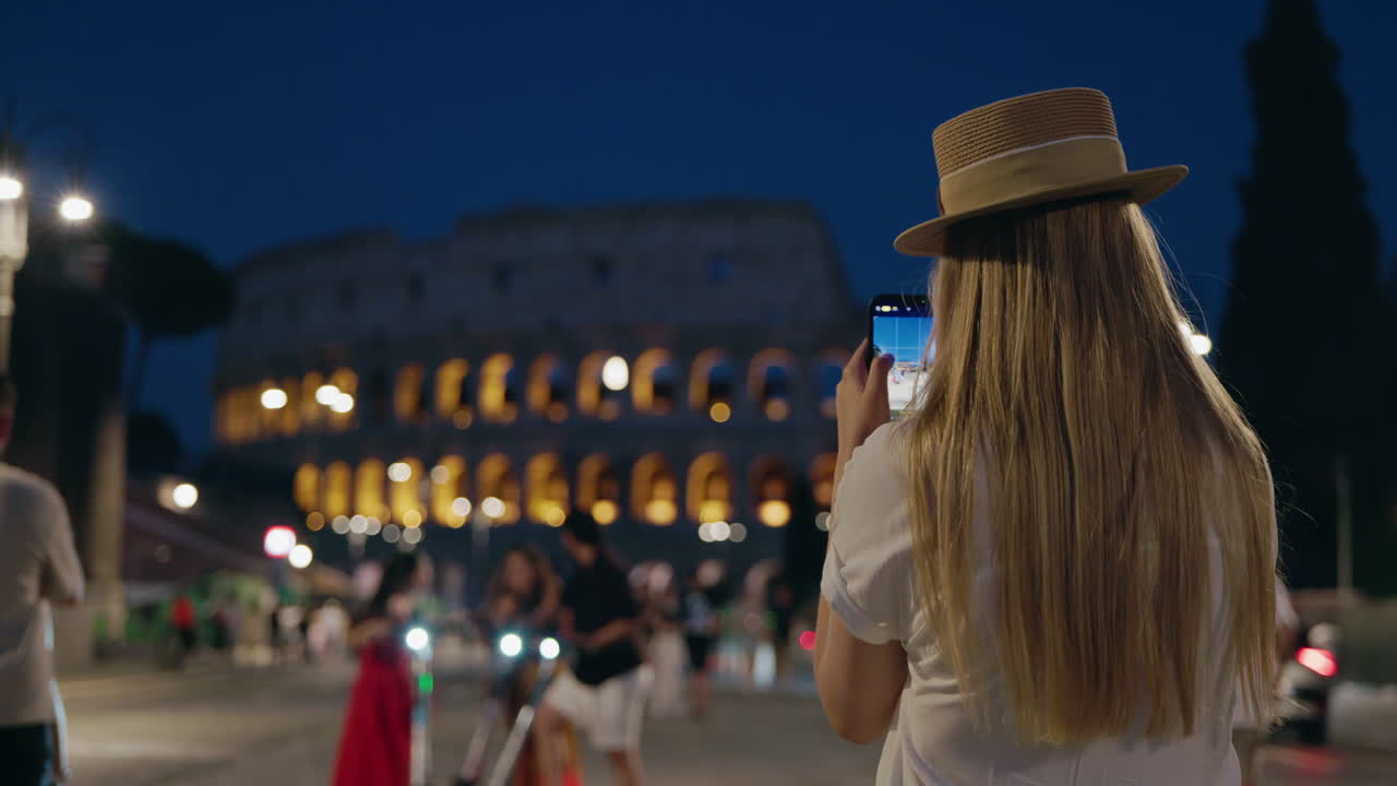 Donna che scatta una foto del Colosseo a Roma di notte.