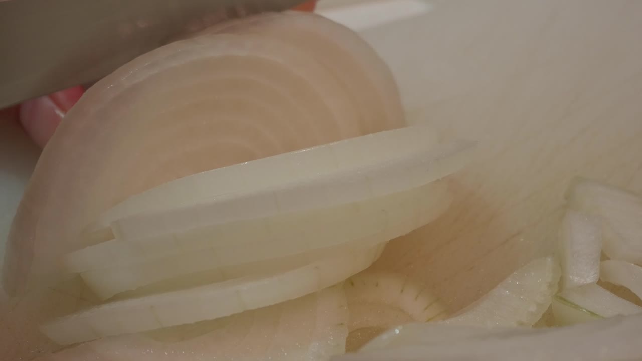 Primo piano di una cipolla che viene affettata, focus su texture e freschezza in cucina