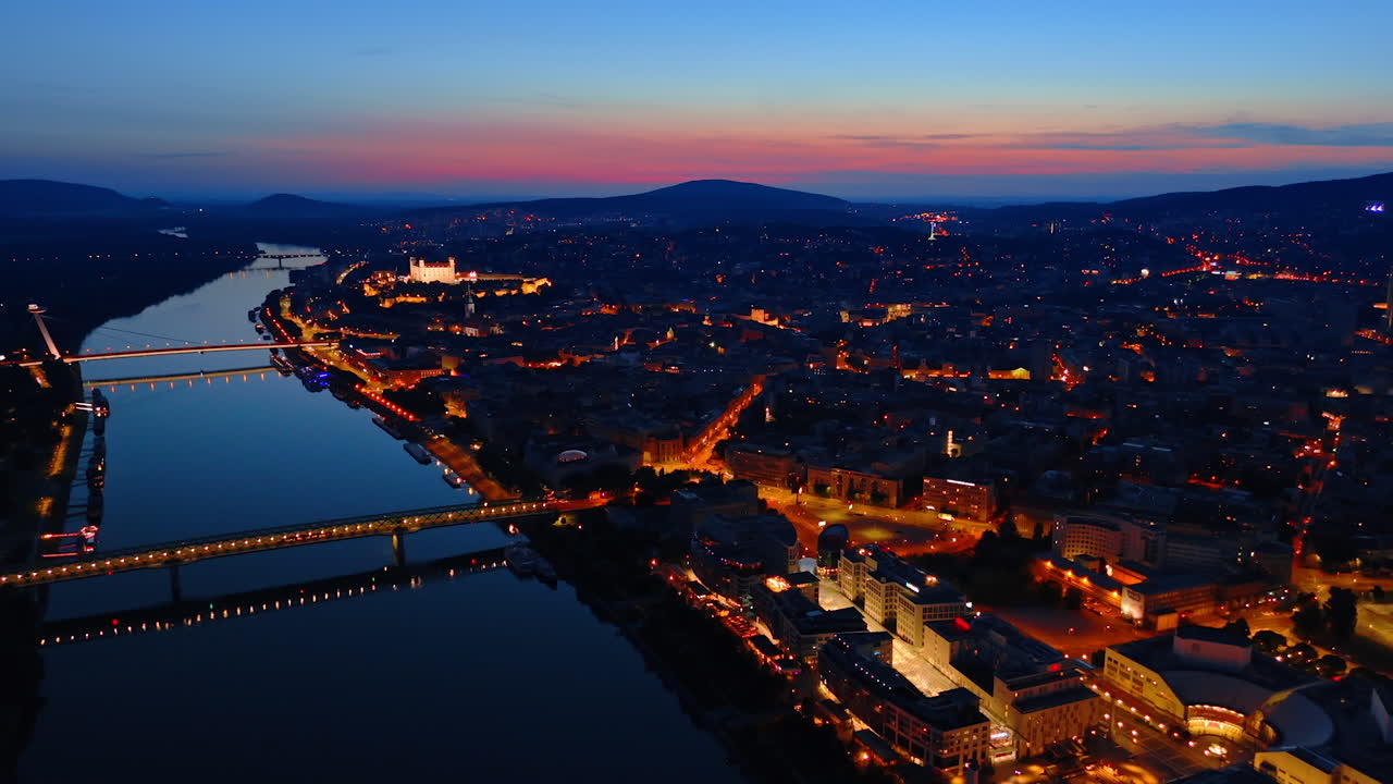 Bratislava, Slovakia - June 14, 2025: Night view of Bratislava along the river. Bratislava shines at night with illuminated buildings and bridges reflecting on the river against a dusk sky