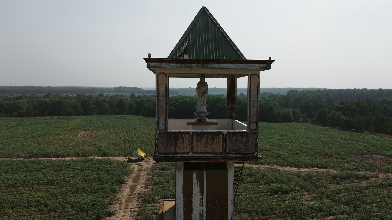 Weathered statue atop an abandoned structure in Tay Ninh, South Vietnam, with vast fields