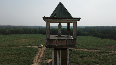 weathered statue atop an abandoned structure in tay ninh, south vietnam, with vast fields