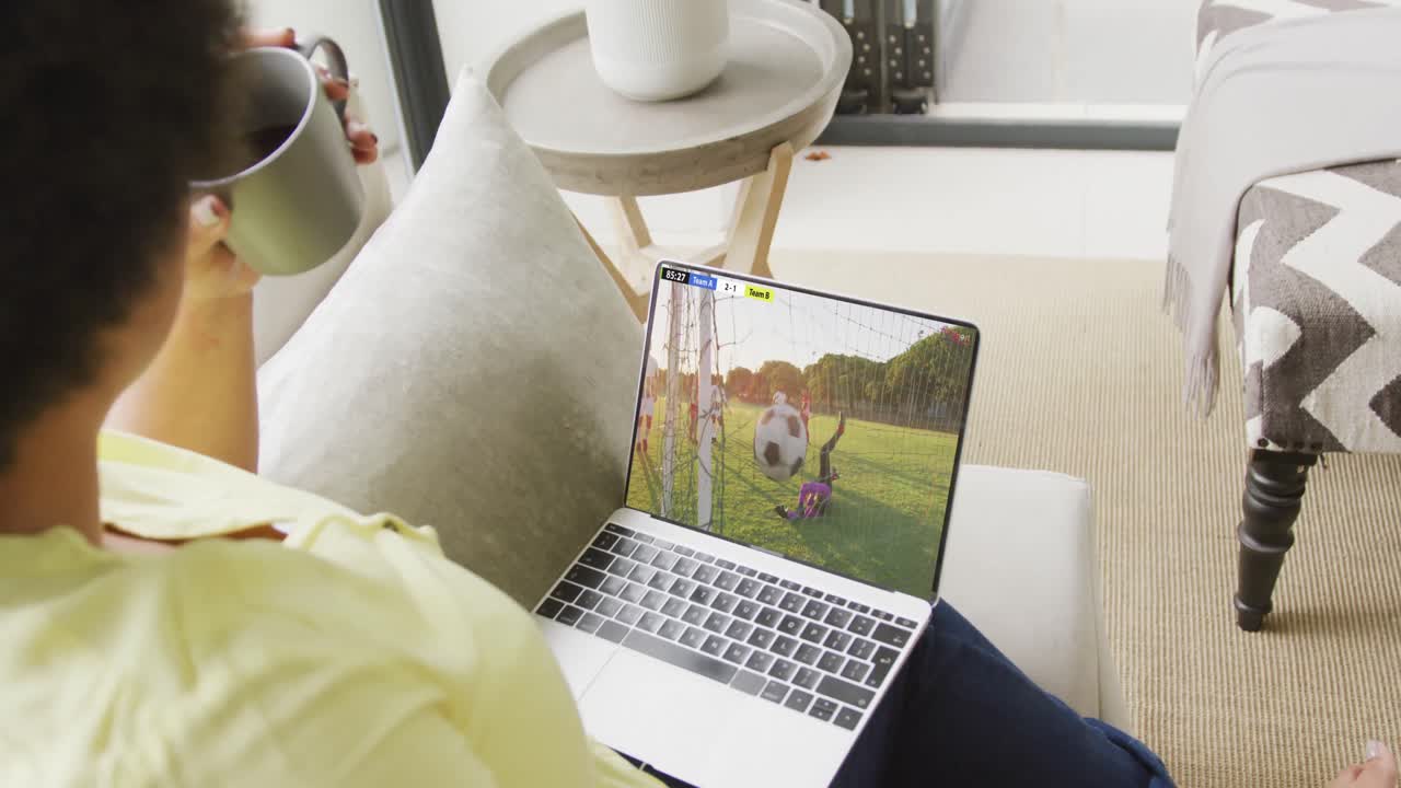 African american woman using laptop with diverse male soccer players playing match on screen