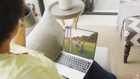 mujer afroamericana usando una computadora portátil con varios jugadores de fútbol masculino jugando un partido en la pantalla