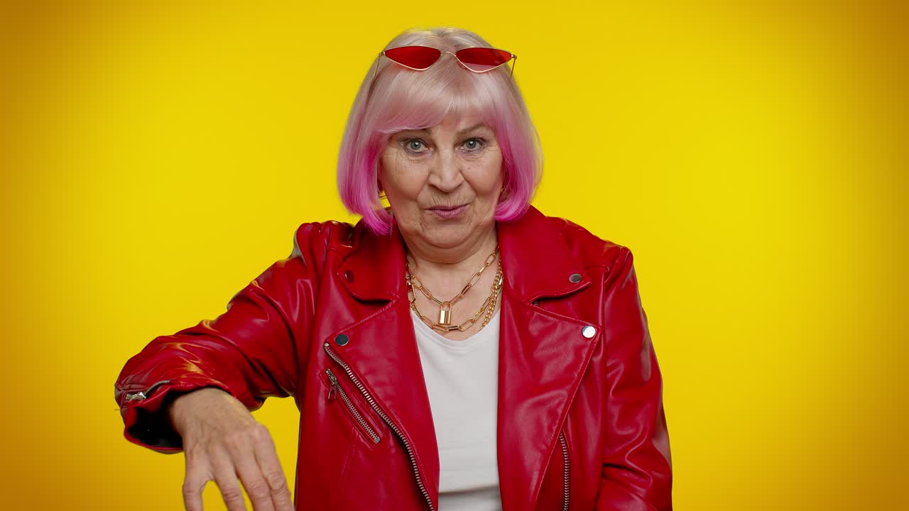 Anziana donna dai capelli grigi che guarda in camera e fa il gesto del telefono, come per dire 'ehi, richiamami'.