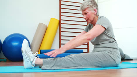 elderly woman touching her toes on exercise mat