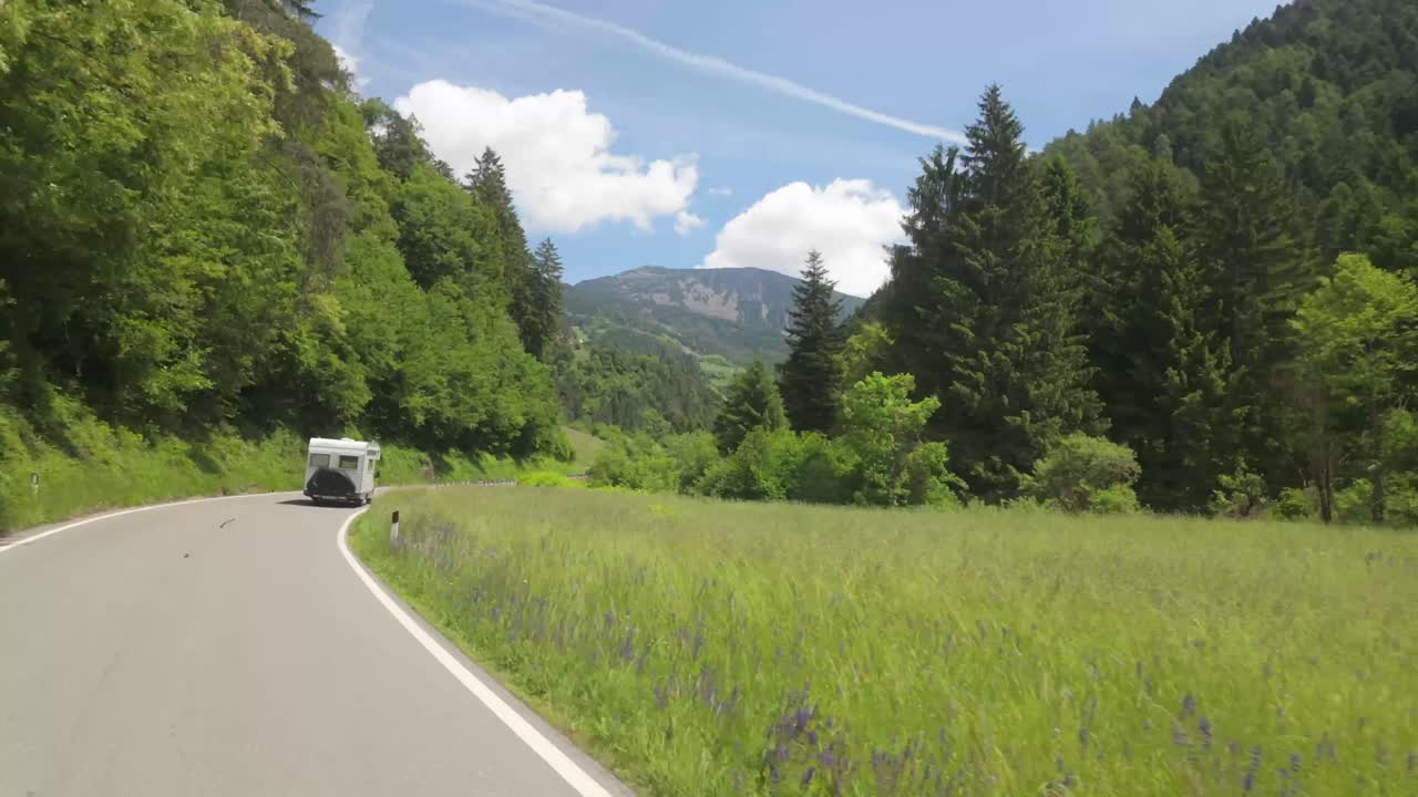 Camera tracks a campervan driving through lush green meadows in the Italian Alps, heading toward the majestic Dolomites.