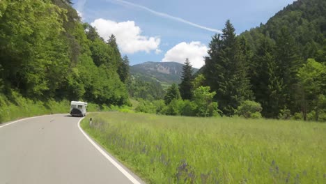 camera tracks a campervan driving through lush green meadows in the italian alps, heading toward the majestic dolomites.