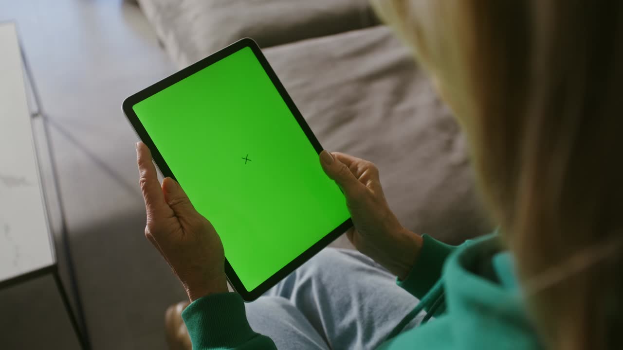 mujer mayor sonriendo comenzando una llamada de video en una tableta sentada en un sofá