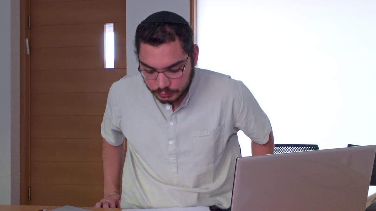 Young Jewish Man with Beard Analyzing a Business Report with Laptop