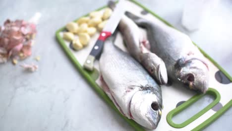 hand peeling garlic next to a sea bream and a whiting on the work surface