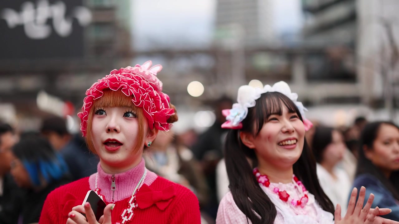 Kaksi nuorta naista kirkkaan vaaleanpunaisessa decora-katutyylissä juttelee ja hymyilee Harajukussa, Tokiossa.