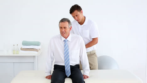 Stressed-businessman-getting-his-back-checked-by-physiotherapist