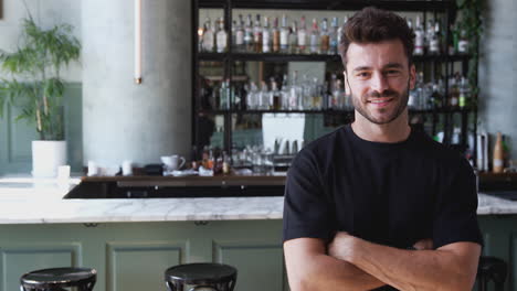 portrait of confident male owner of restaurant bar standing inside by counter