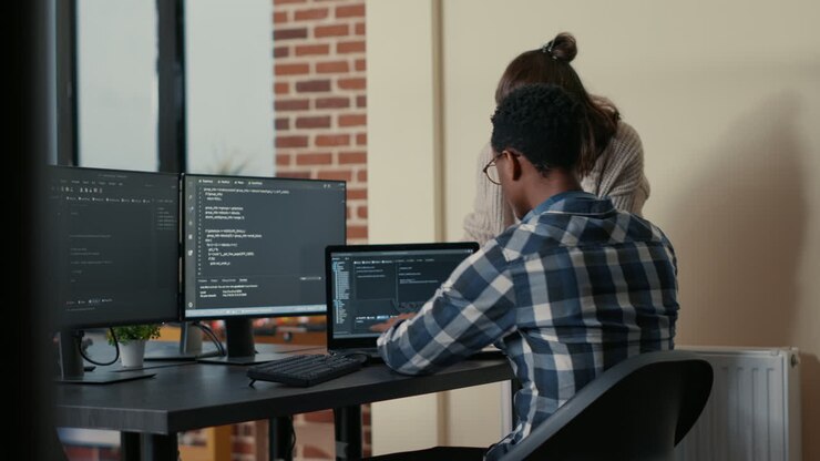 Two programmers doing high five hand gesture at desk with multiple screens running code celebrating