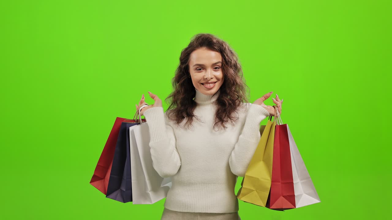 The woman is looking at the camera and smiling. She is picking up the shopping bags. She is standing on a green background. Green screen. 4K.