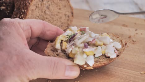 A-man-puts-a-vegetable-salad-on-a-piece-of-bread-and-adds-a-sprig-of-dill-on-a-wooden-cutting-board