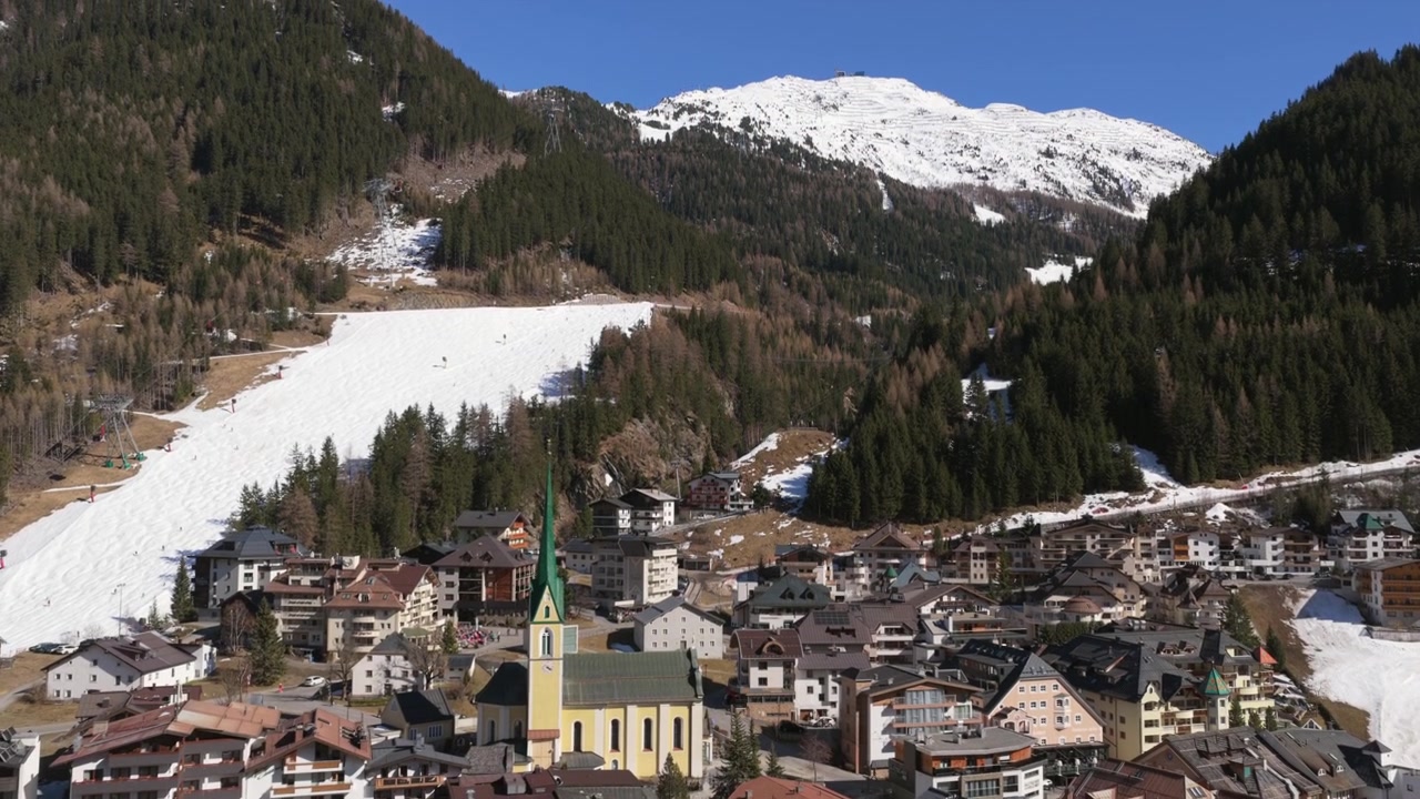 Villaggio di Ischgl in Tirolo, Austria, con chiesa dalla guglia verde e stazione sciistica in una giornata di sole. Ripresa aerea con movimento tilt-up.