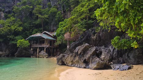 Isla-Tropical-Desierta,-Casa-Rústica-De-Madera-Bajo-Acantilados-De-Piedra-Caliza,-Playa,-árboles-Y-Mar-Turquesa