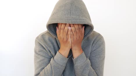 man in a hoodie covering his face with his hands